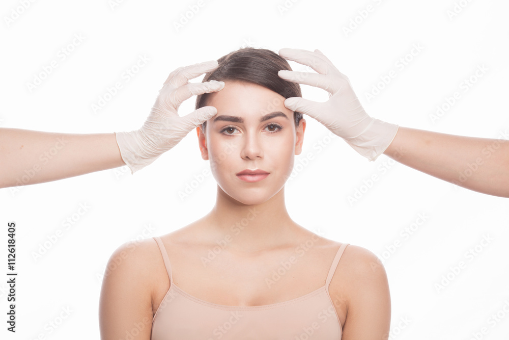 Handmade beauty. Beautiful young woman keeping eyes opened while two hands in medical gloves touching her face isolated on white background. Handmade beauty. Beautiful young woman keeping eyes opened while two hands in medical gloves touching her face isolated on white background.