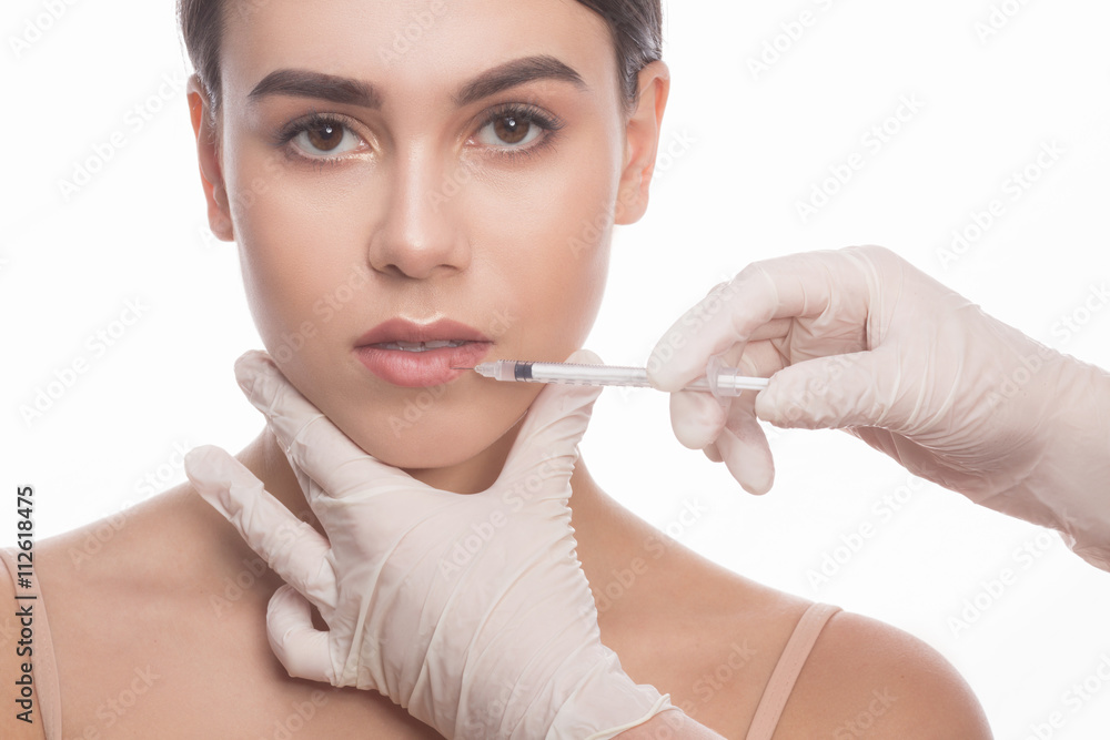 Closeup of beautiful woman getting injections in her lips. Beautiful face and syringe. Plastic surgery and cosmetic injection concepts. Full lips. Closeup of beautiful woman getting injections in her lips. Beautiful face and syringe. Plastic surgery and cosmetic injection concepts. Full lips.
