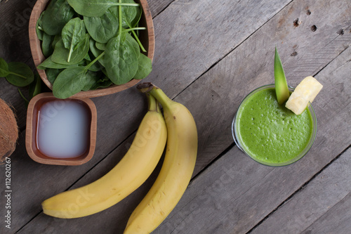 A glass of green smoothies, and the ingredients from which it was made. Smoothies with spinach, banana, coconut water, pineapple on gray wooden table.