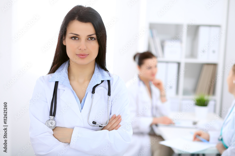 Brunette female doctor on the background of colleagues talking to each other in hospital Brunette female doctor on the background of colleagues talking to each other in hospital