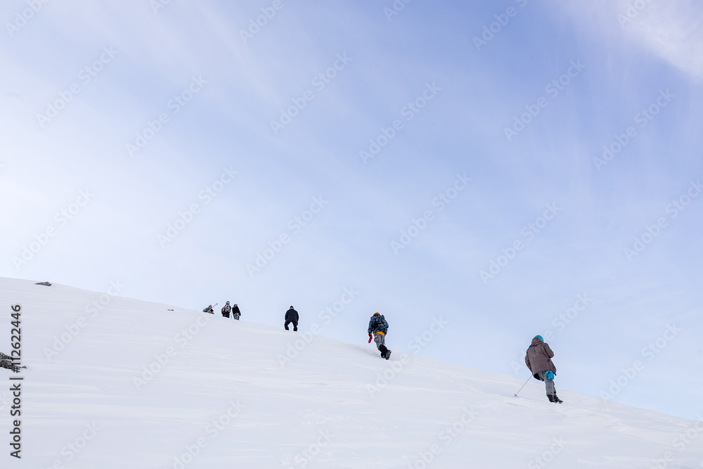 mountaineering group of tourists climbing up the snow covered mountain. The steep slope and a snowstorm on a clear day