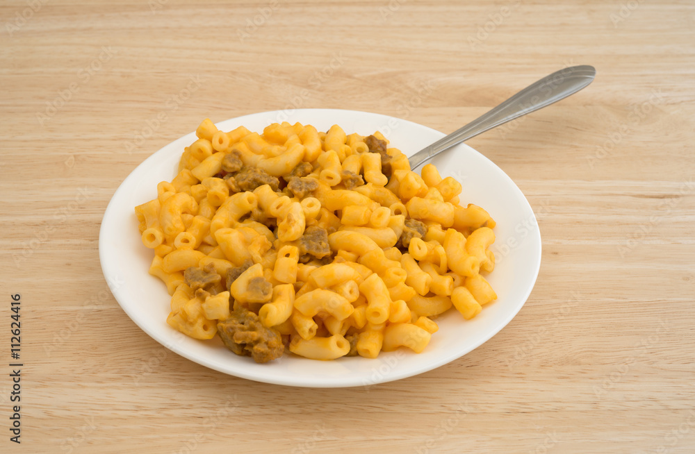Mac and cheese with burger on plate with fork atop a wood table top side view Mac and cheese with burger on plate with fork atop a wood table top side view