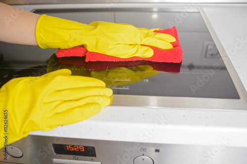 Blond girl in the yellow gloves with sponge wiping down ceramic heating surface