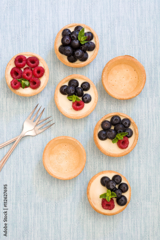 Delicious tartlets with raspberries and blueberries on blue background
