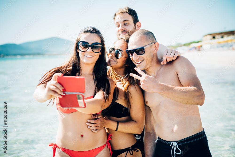 Group of young multiethnic friends women and men at the beach in summertime taking selfie in the water, having fun, smiling - friendship, smiling, happiness, vanity, social network concept