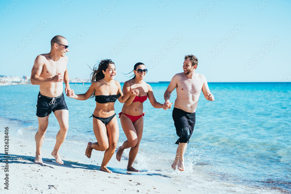 Group of young multiethnic friends women and men running on the seashore hand in hand, having fun, laughing- friendship, summertime, happiness concept Group of young multiethnic friends women and men running on the seashore hand in hand, having fun, laughing- friendship, summertime, happiness concept
