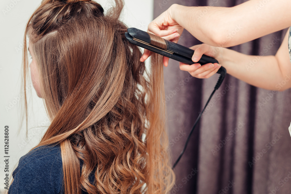 Fototapeta premium Golden-haired blonde doing the Curling irons in the beauty salon