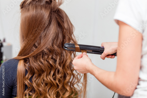 Stylist curling hair for brown haired woman. Girl care about her hairstyle