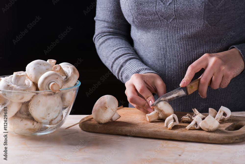 female hands cutting fresh mushrooms on the wooden desk