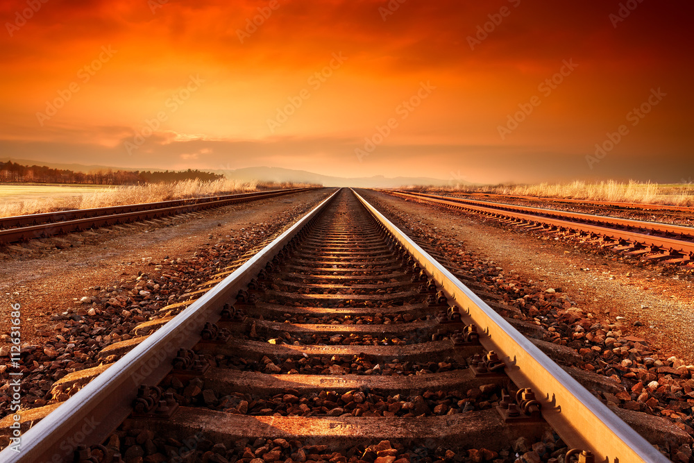 Fototapeta premium Tory kolejowe idą na horyzont w majestatycznym zachodzie słońca.