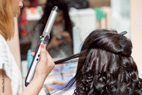 Stylist in barber salon using curling iron for brunette hair curls, close-up