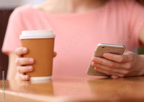 Young woman sitting in cafe with coffee and smartphone