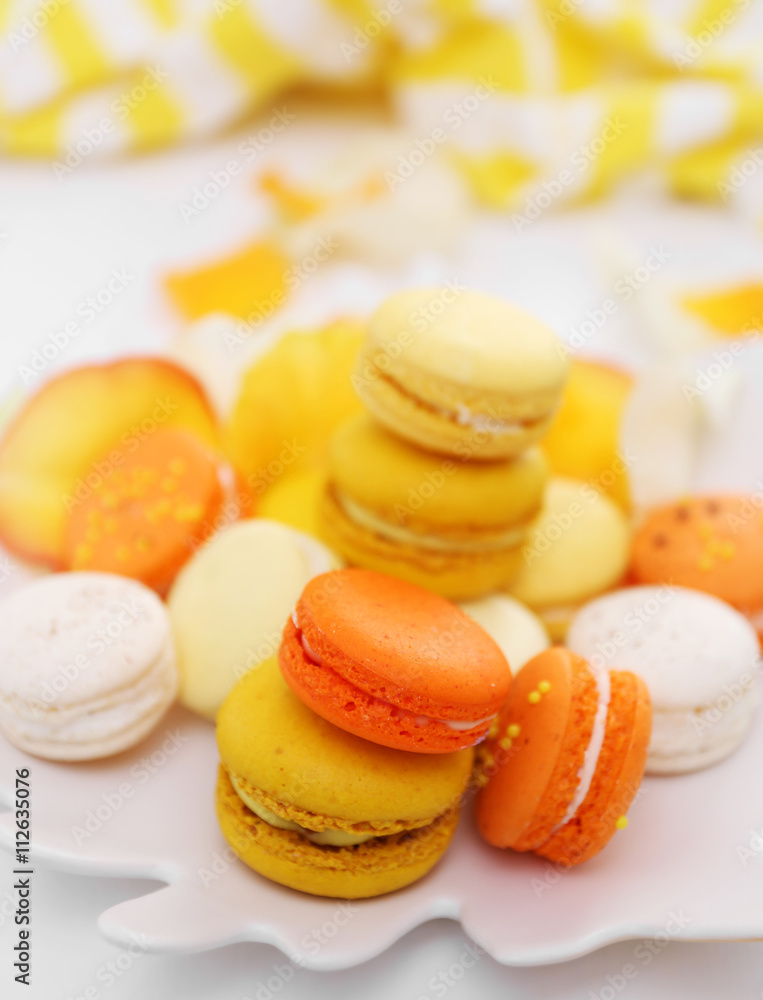 Plate with fresh macaroons and rose petals on light background