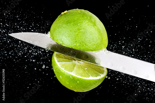Lemon chopped by knife in mid air, black background