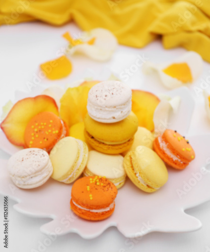 Plate with fresh macaroons and rose petals on light background