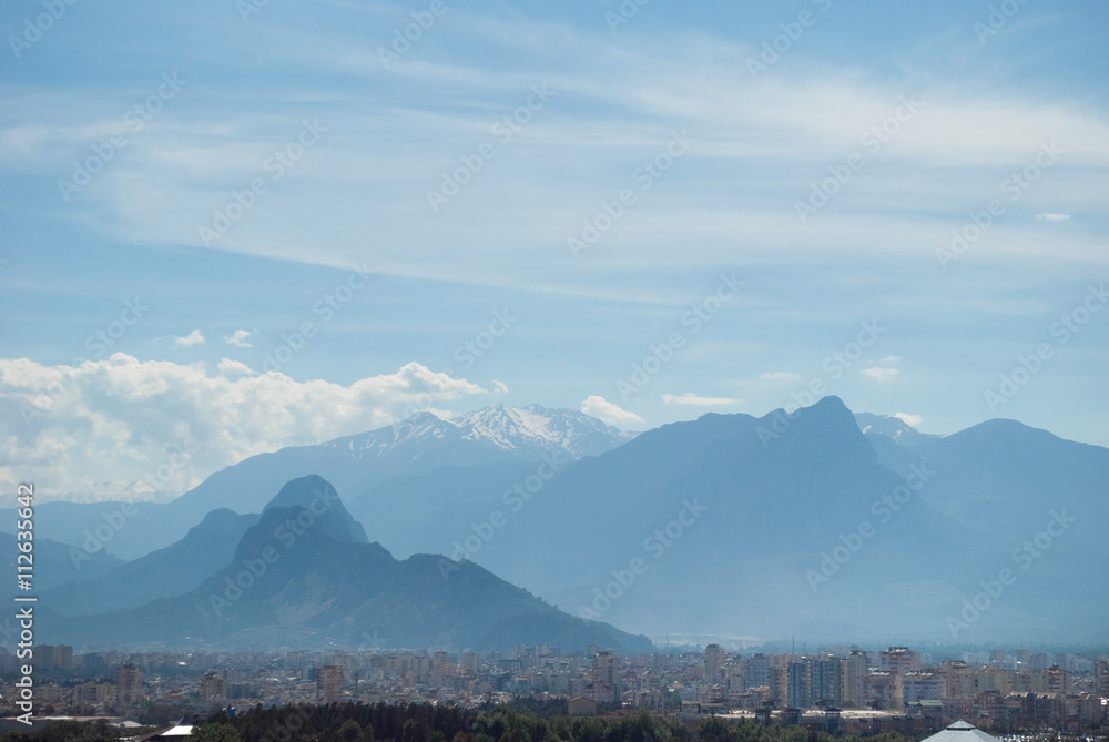 City and mountains background. Sunny landscape with blue sky