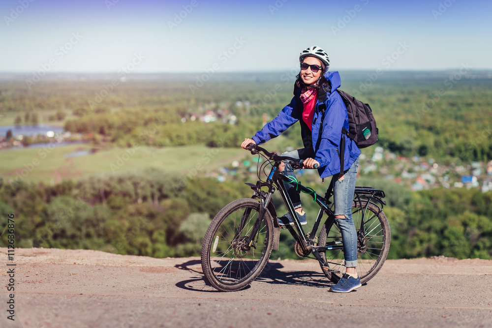 Young woman cyclist with backpack in helmet riding in the park