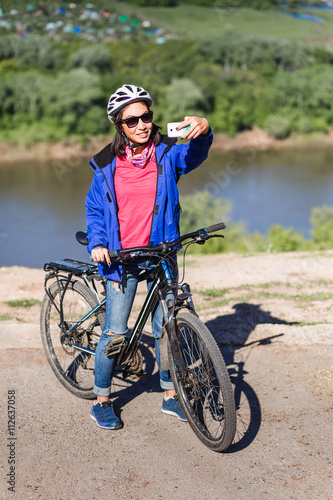 Adult attractive female cyclist stand near bicycle and makes the