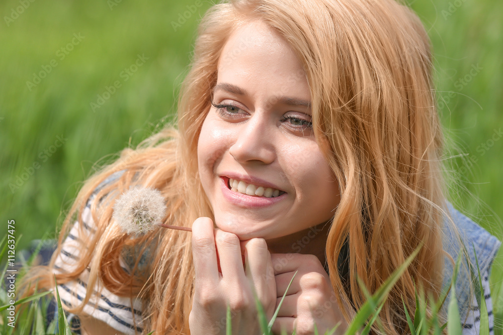 Naklejka premium Young beautiful woman with blowball on green grass