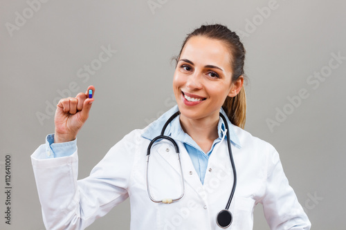 Portrait of beautiful female doctor looking at camera and holding bottle of pills. 