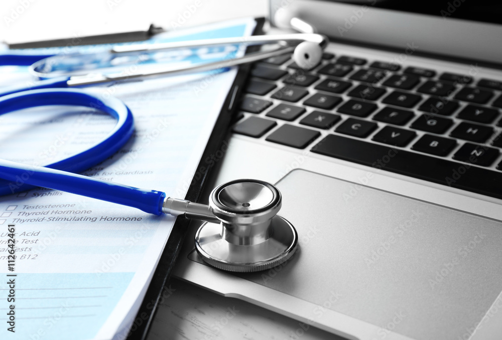 Stethoscope with medical form and laptop, close-up Stethoscope with medical form and laptop, close-up