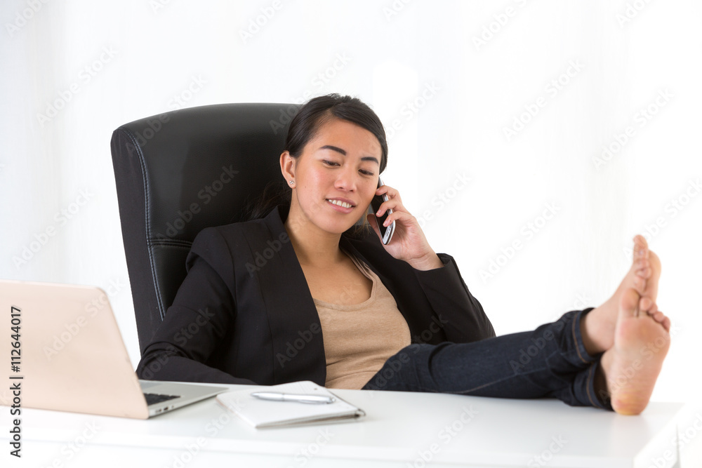 Asian employee relaxing at phone with feet on desk Asian employee relaxing at phone with feet on desk