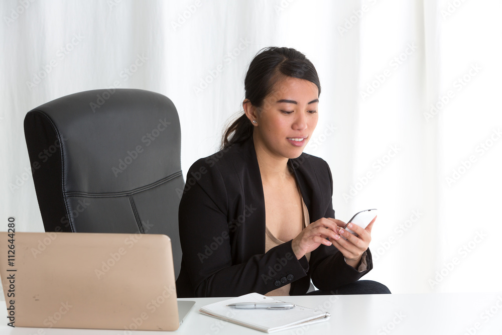 Asian employee typing on her telephone sitting at desk in office Asian employee typing on her telephone sitting at desk in office