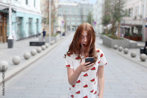 Front view of a fashion happy girl walking and using a smart pho