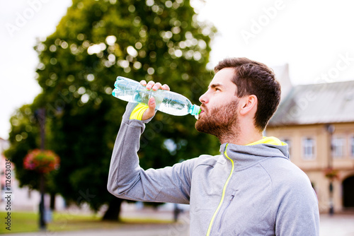 Young hipster runner in town with water bottle, drinking