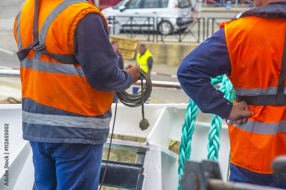 hommes de service d'un bateau de transport avec gilet orange tenant ligne de mouillage
