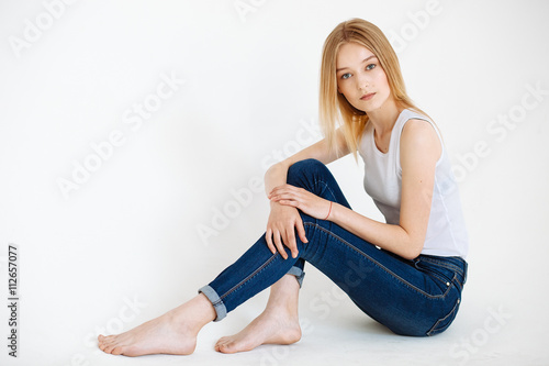 Young European woman posing in studio for test photo shoot showing different poses sitting on white seamless background