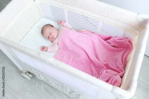 Lovely newborn girl sleeps in travel crib