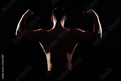 Back of athletic man showing muscles on black background © ArtFamily