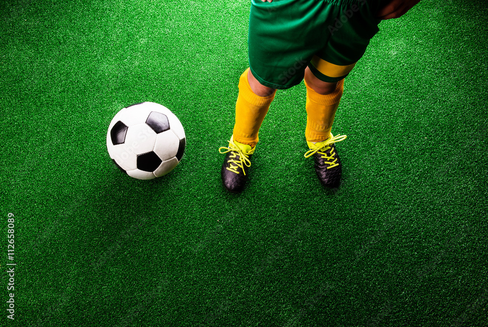 Obraz premium Unrecognizable little football player against green grass, studi