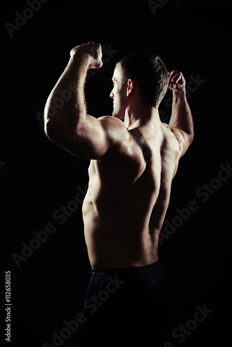 Handsome man is showing muscles on black background