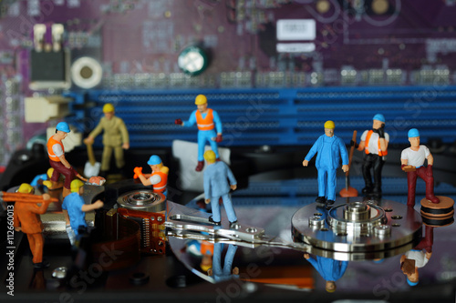 Selective focus of miniature engineer and worker meeting, maintenance hard disk and fixed problem hard disk of Personal computer (PC) on blurred mainboard background as industrial concept.