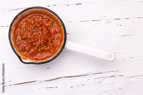 Stieltopf mit Sauce Bolognese auf weißem Hintergrund aus Holz, photo