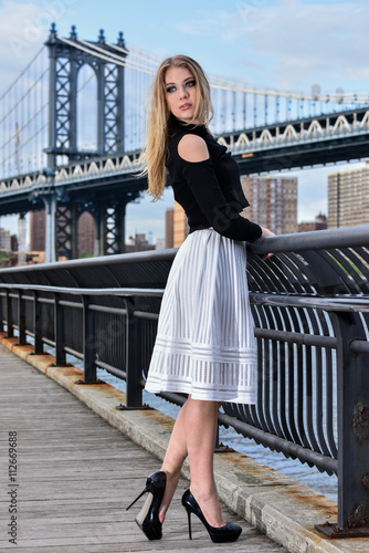 Attractive blond fashion model posing pretty on the pier with Manhattan Bridge on the background, New York City. © FashionStock