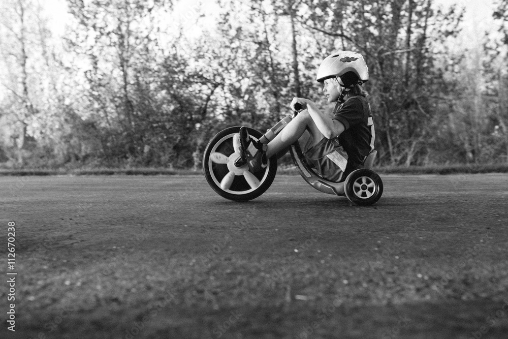 Young boy riding tricycle outdoors, low angle view, black and white Young boy riding tricycle outdoors, low angle view, black and white