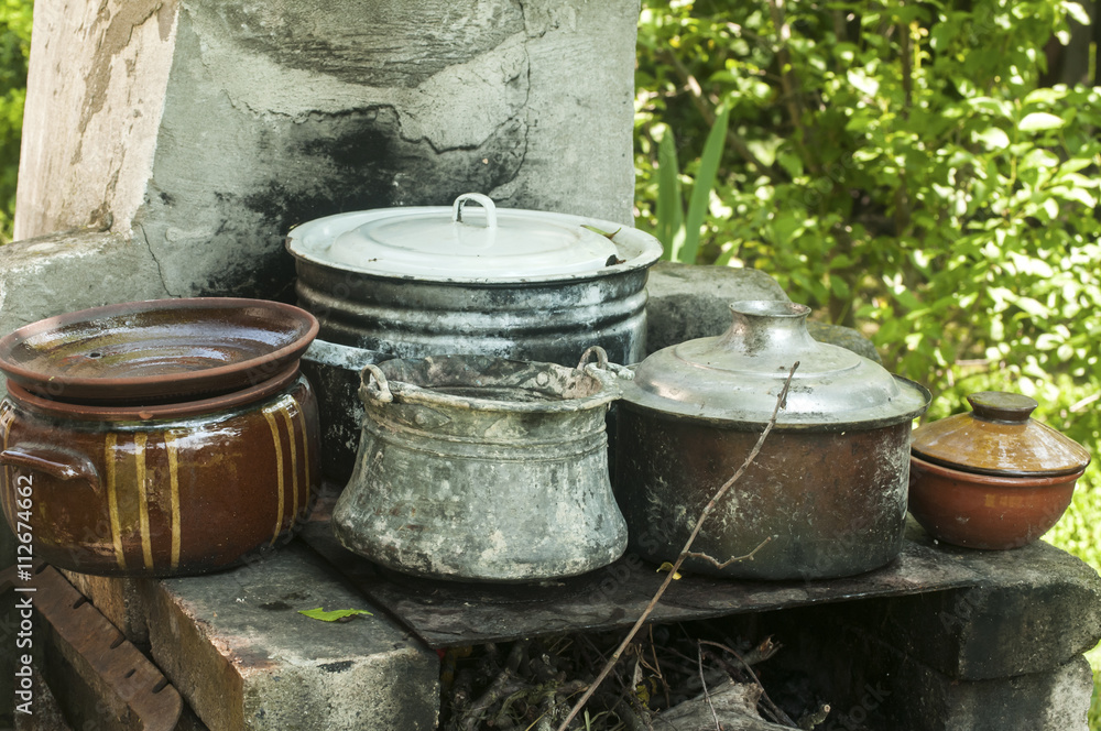 Outdoor fireplace in rural yard with stacks of old metal pots and clay cookware