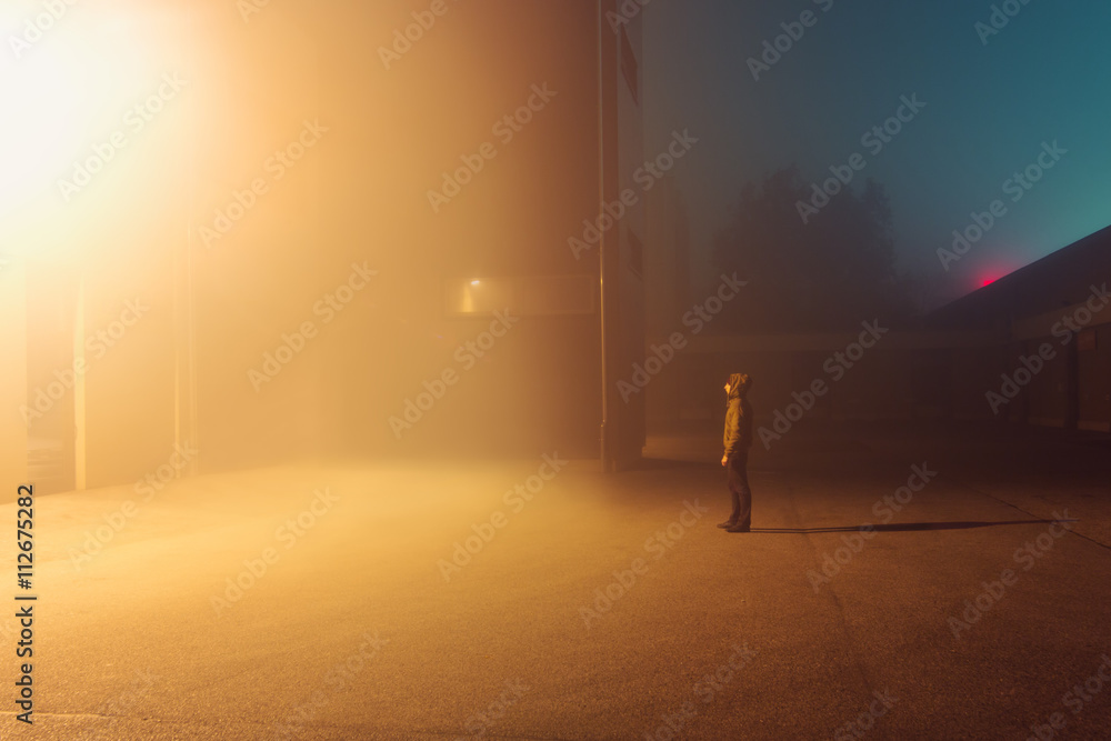 Man standing outside building in fog at night Man standing outside building in fog at night
