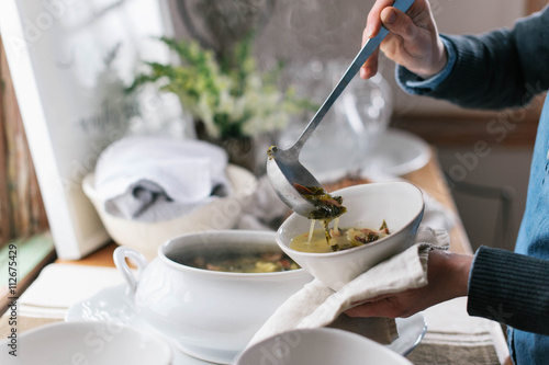 Hands of person serving soup in a bowl with ladle photo