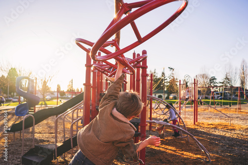 Rear view of boy swinging on monkey bars in playground photo