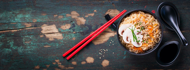 Asian noodles with vegetables and mushrooms, soy sauce, sticks on a dark background, top view with copy space 
