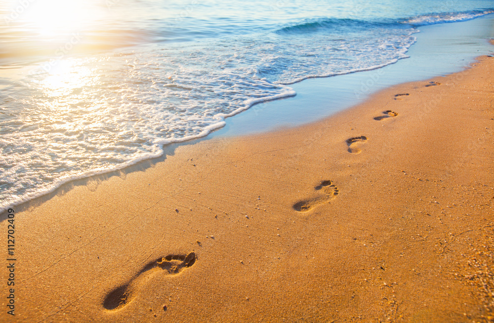 Naklejka premium plaża, fala i ślady stóp w czasie zachodu słońca