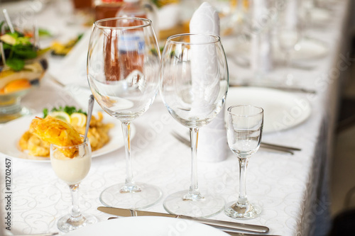 Settings for celebration. Table served with different food and flatware. Beautiful table ready for guests. Empty clean glasses and plates on festive table. Horizontal color photo