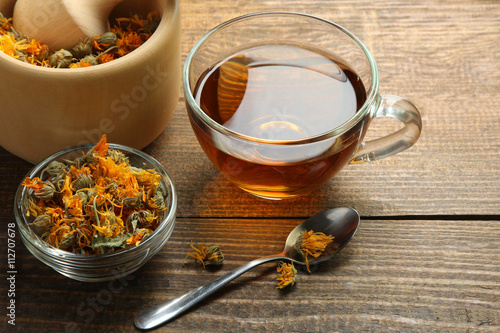 the dried flowers  calendula in a wooden Mortar  on wooden brown background with Cup of tea