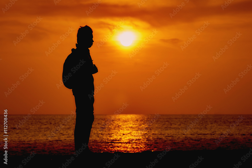 Silhouette of a traveler with a backpack standing on the shore of Kata beach in Phuket during the sunset.