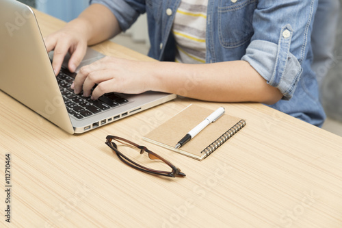 woman using laptop computer with eyeglasses, notebook and pen