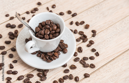 Cup of coffee beans with a spoon and saucer on a white background with the outline of more coffee beans